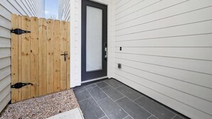 A house exterior with a wooden fence, a dark-colored door, and a tiled driveway. - Designer 3BR w/ Fireplace, Yard & Free Parking (Houston)