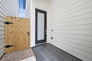 A house exterior with a wooden fence, a dark-colored door, and a tiled driveway. - Designer 3BR w/ Fireplace, Yard & Free Parking (Houston)