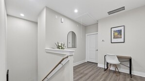 A modern interior with a staircase, a white wall, a framed picture, and a desk with a chair. - Designer 3BR w/ Fireplace, Yard & Free Parking (Houston)