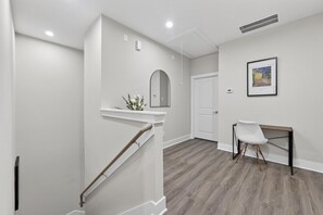 A modern interior with a staircase, a white wall, a framed picture, and a desk with a chair. - Designer 3BR w/ Fireplace, Yard & Free Parking (Houston)