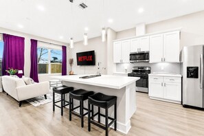 A modern kitchen with white cabinets, a central island with bar stools, a microwave, and a refrigerator. - Designer 3BR w/ Fireplace, Yard & Free Parking (Houston)