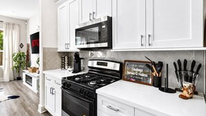 A modern kitchen with white cabinetry, a black stove, a microwave, and a coffee maker. - Gated Community Texas Style  3BR + Private Parking (Houston)