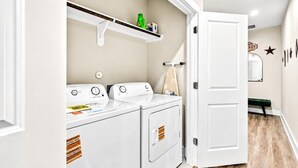 A laundry area with a washing machine, dryer, and a shelf above the dryer. - Gated Community Texas Style  3BR + Private Parking (Houston)