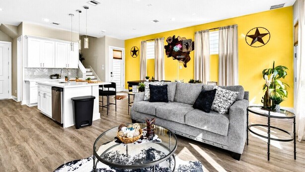 A modern living space with a kitchen, a grey sofa, and a coffee table. - Gated Community Texas Style  3BR + Private Parking (Houston)