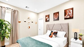A bedroom with a bed, a nightstand, a lamp, a potted plant, and wall art. - Gated Community Texas Style  3BR + Private Parking (Houston)