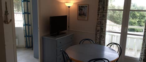 A dining area with a table, chairs, a television on a cabinet, a lamp, and a window with curtains.