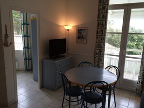 A dining area with a table, chairs, a television on a cabinet, a lamp, and a window with curtains. - Duplex with a balcony, apartment complex with a pool, 5-minute walk to the beach and market (La Couarde-sur-Mer)