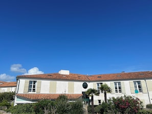 A two-story building with a tiled roof, white walls, and multiple windows with shutters. - Duplex with a balcony, apartment complex with a pool, 5-minute walk to the beach and market (La Couarde-sur-Mer)