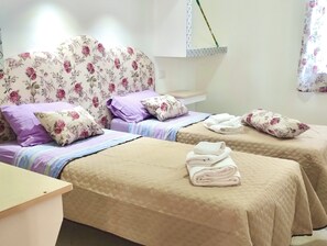 A hotel room with two beds, floral-patterned headboards, and a bedside table with towels. - Residence with swimming pool in Capo Vaticano (Santa Maria)