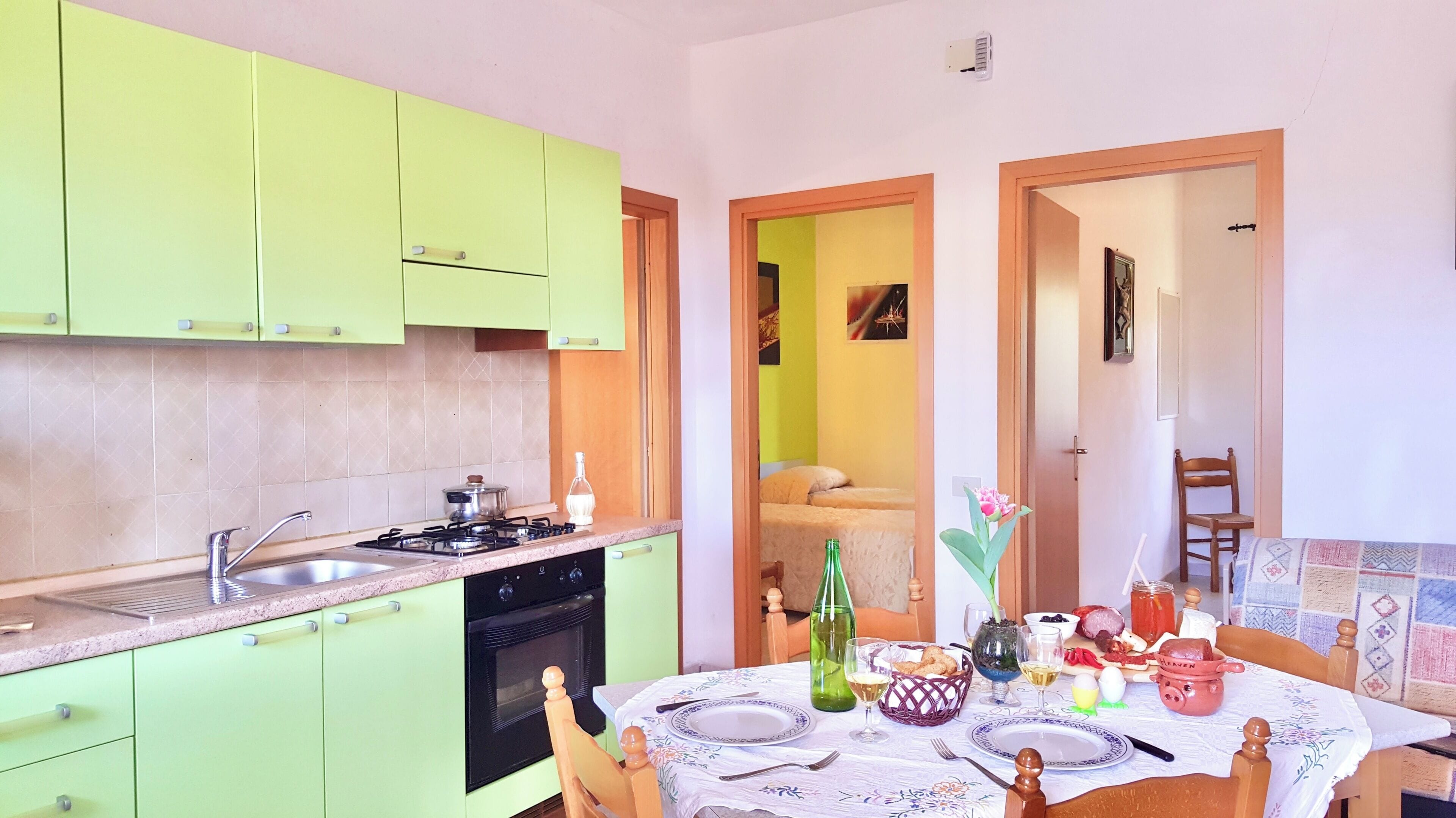 A kitchen with green cabinets, a dining table set with plates, glasses, and a bottle.