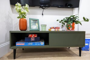 A green entertainment unit with a television mounted above it, a vase with white flowers, a framed picture, and a potted plant. - North End Entire House / Heart of Boston (Boston)
