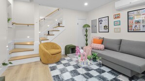 Ein modernes Wohnzimmer mit Treppe, einem grauen Sofa, einem gelben Sessel und einem karierten Teppich.