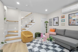 A modern living room with a staircase, a grey sofa, a yellow armchair, and a checkered rug. - North End Entire House / Heart of Boston (Boston)
