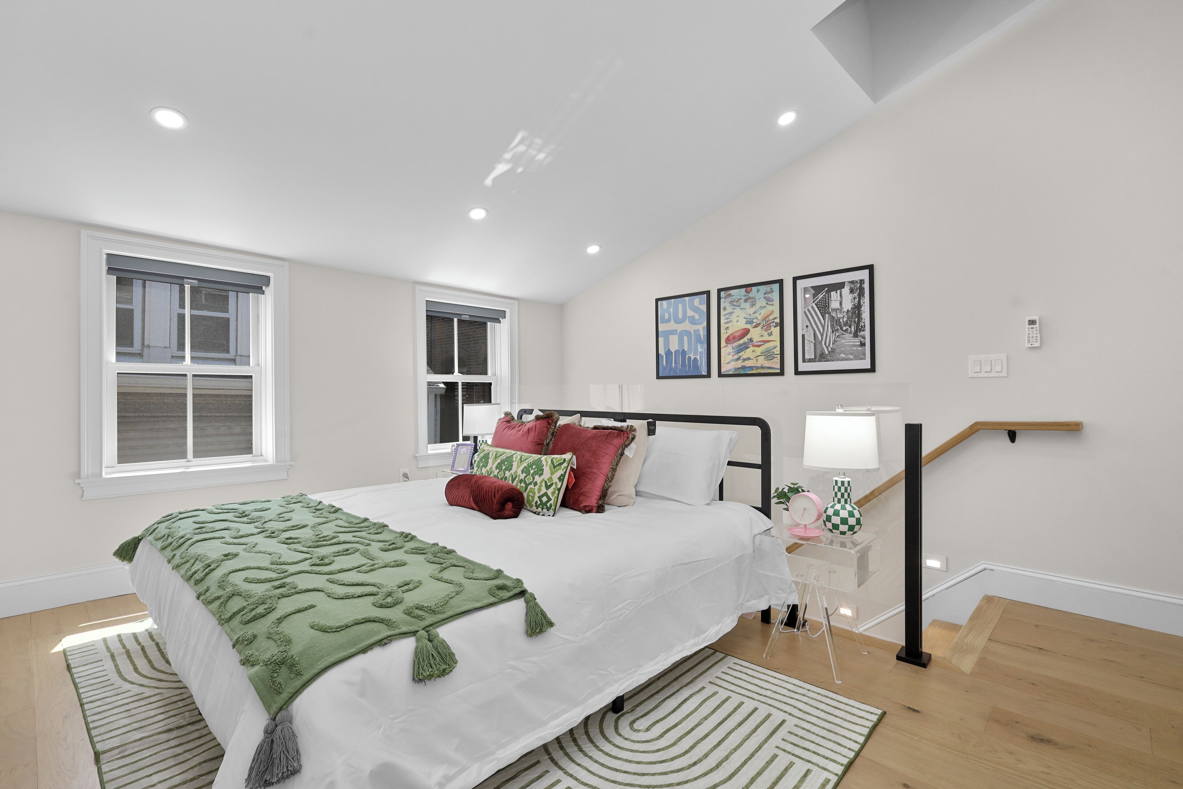 A bedroom with a bed, two windows, a staircase, and wall art.