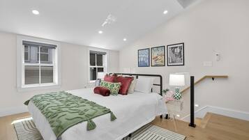 A bedroom with a bed, two windows, a staircase, and wall art.