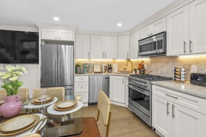 A modern kitchen with white cabinetry, stainless steel appliances, and a dining area set for four. - North End Entire House / Heart of Boston (Boston)