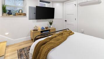Ein Schlafzimmer mit einem Bett, einem Fernseher, einem Nachttisch, einem Fenster und einer Klimaanlage.