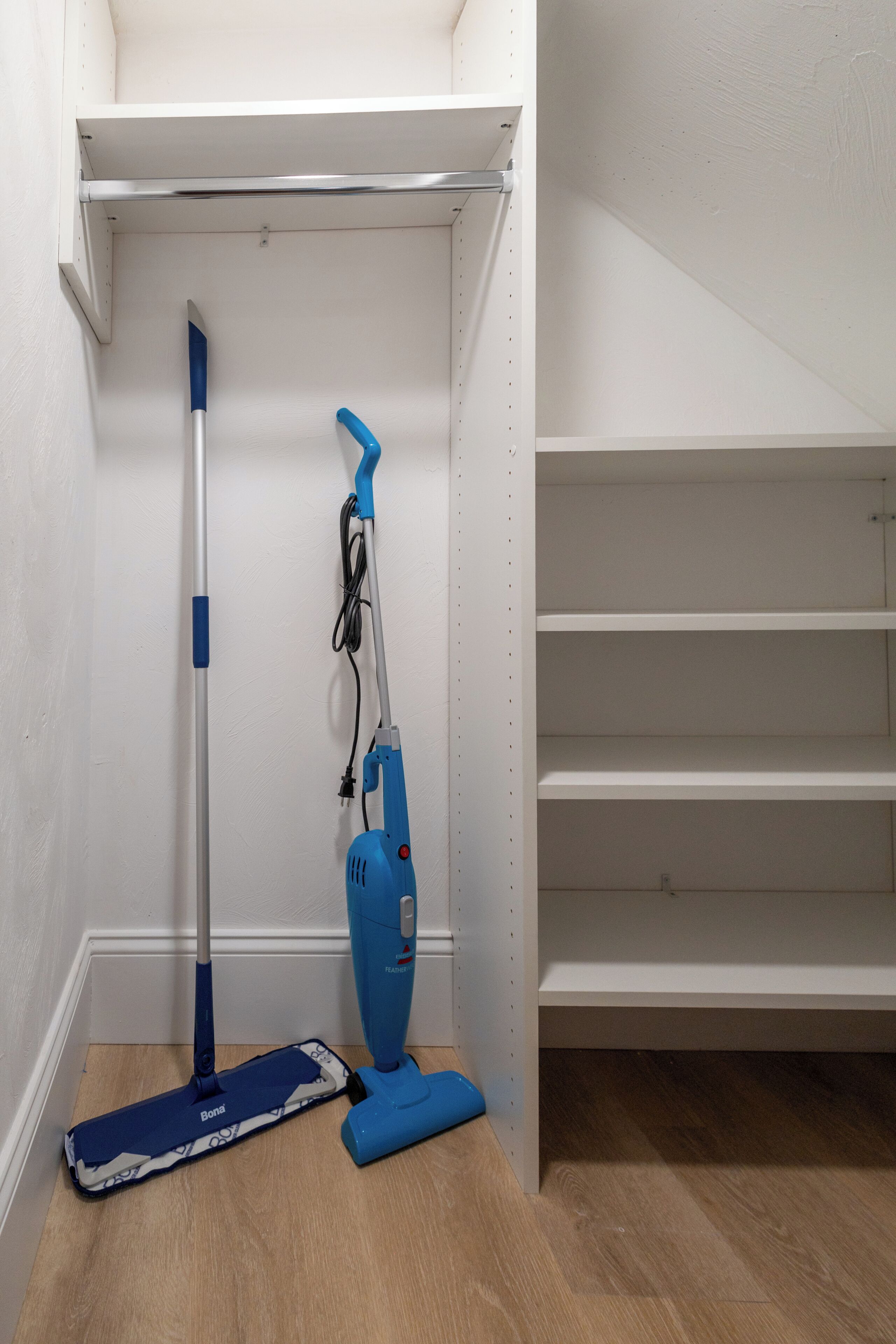A corner of a room with a mop and a vacuum cleaner leaning against the wall.