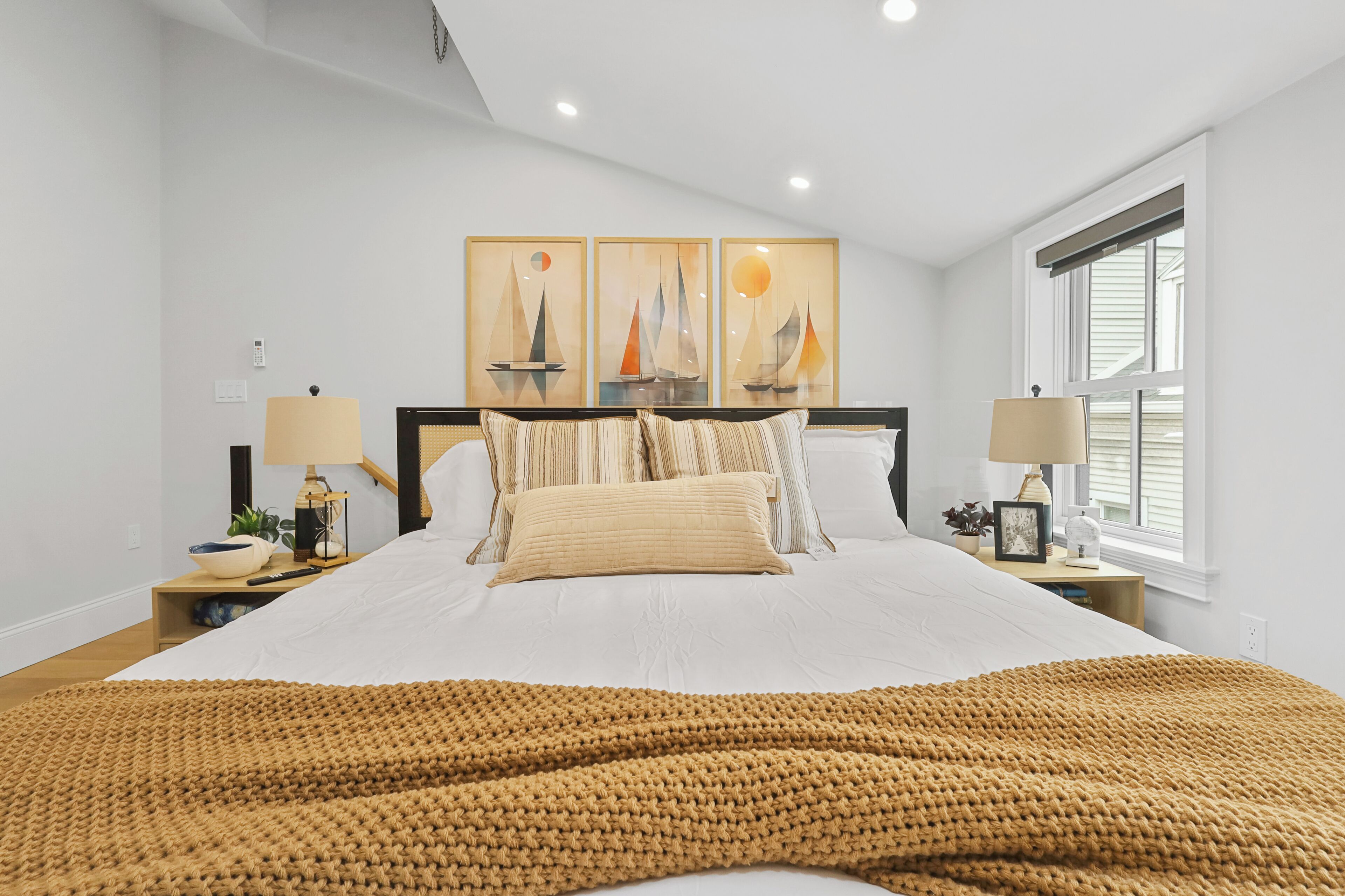 A bedroom with a large bed, two bedside tables, a window, and a wall with three paintings.