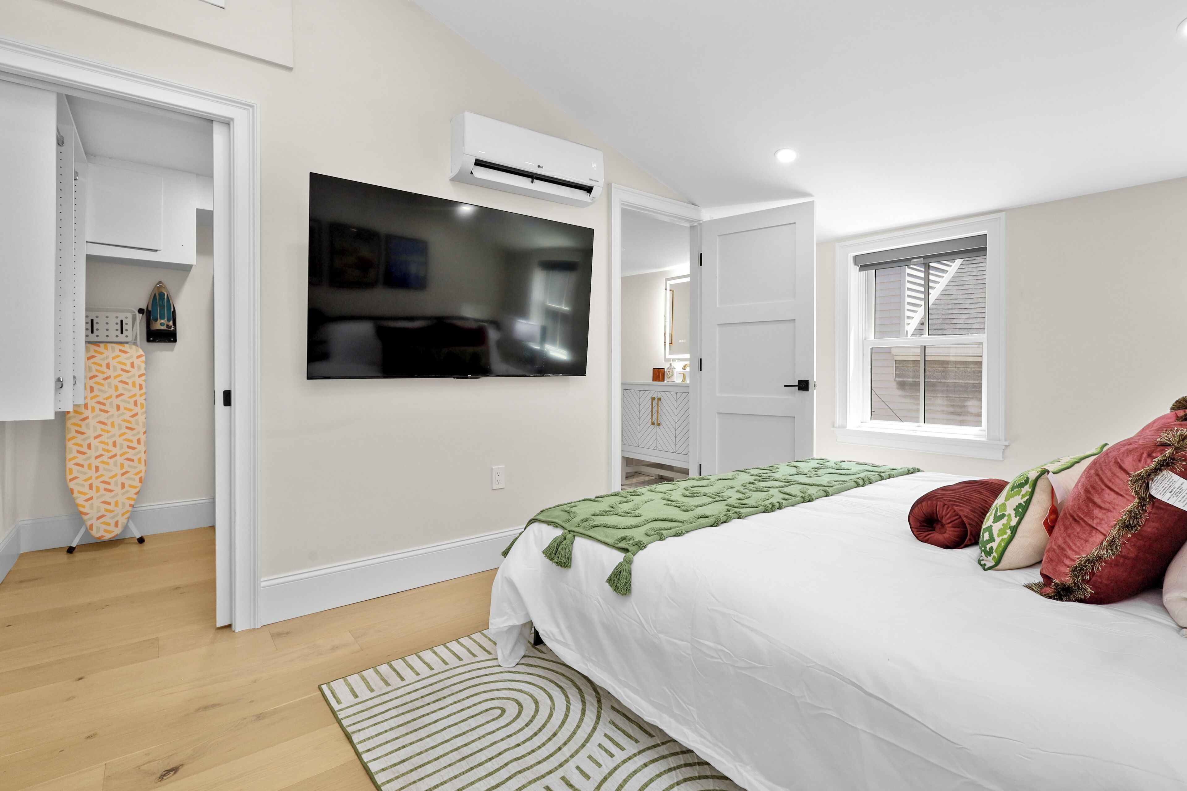 A bedroom with a bed, a television mounted on the wall, and a window.