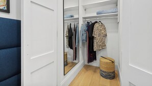 Ein begehbarer Kleiderschrank mit einer spiegelnden Schiebetür, Holzboden und einer blau gepolsterten Bank.