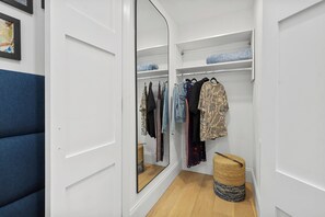 A walk-in closet with a mirrored closet door, wooden flooring, and a blue upholstered bench. - North End Entire House / Heart of Boston (Boston)