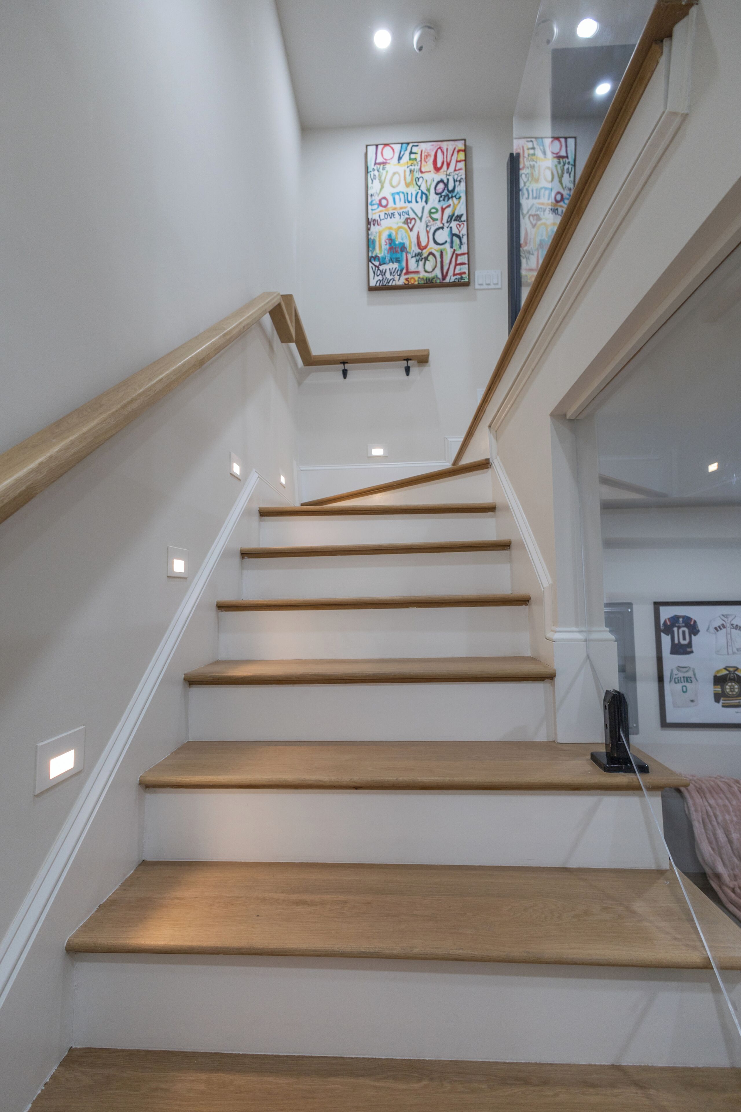 Eine Treppe mit Holzstufen und Geländer, die zu einer Empore mit einem an der Wand befestigten Kunstwerk führt.