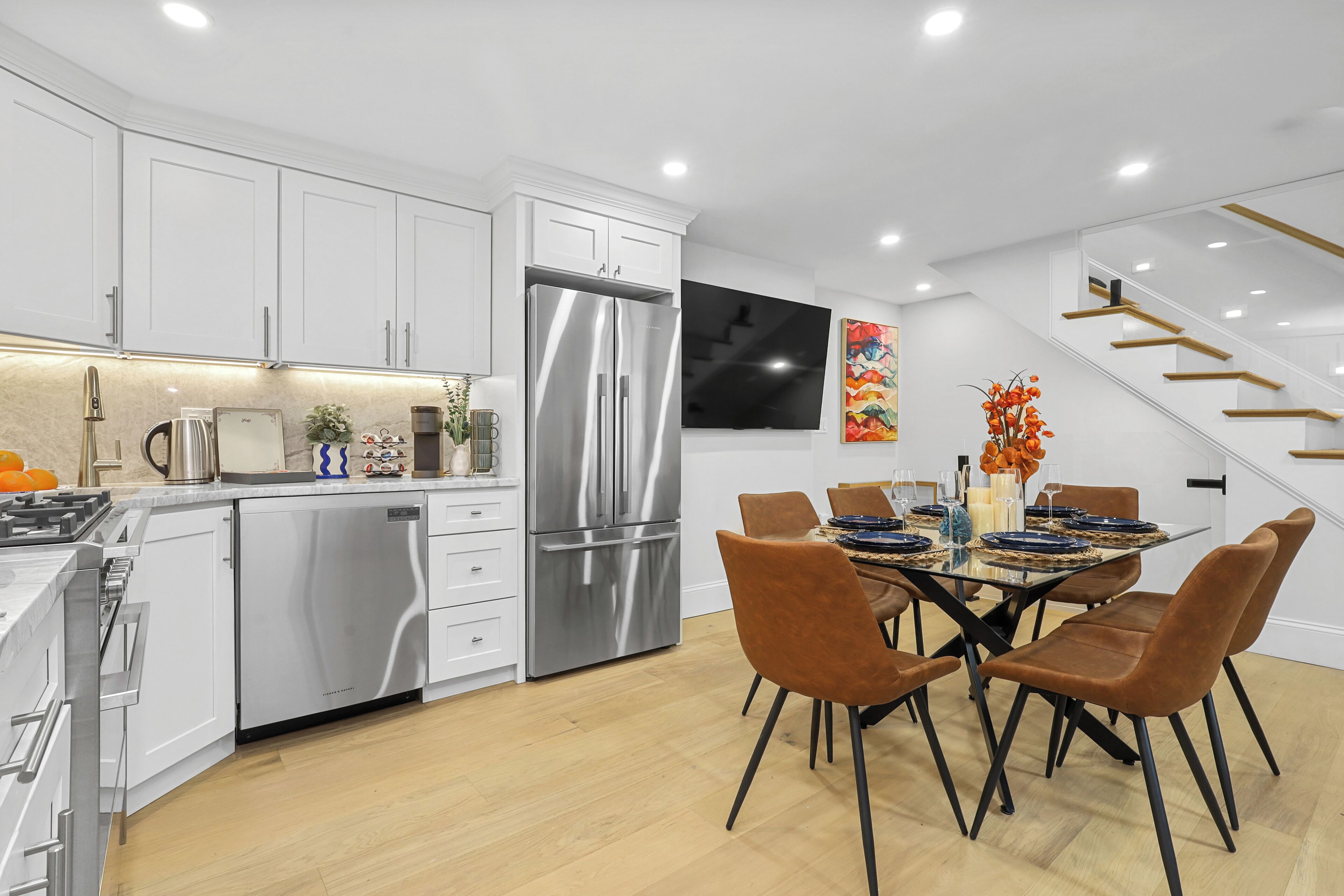 A modern kitchen with white cabinets, stainless steel appliances, and a dining area with a glass table and brown chairs.
