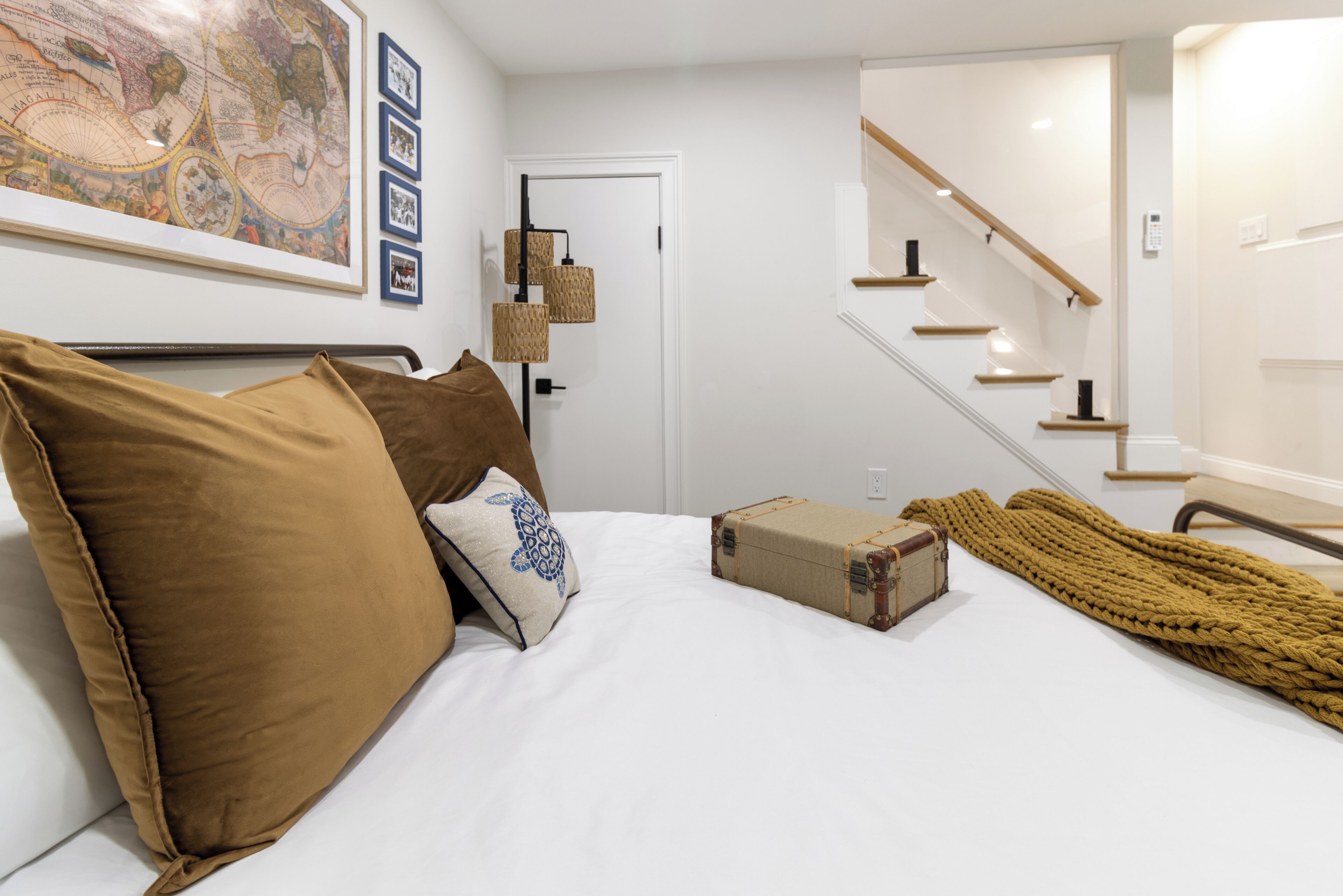 Een slaapkamer met een bed, kussens, een kaart, een koffer en een trap.