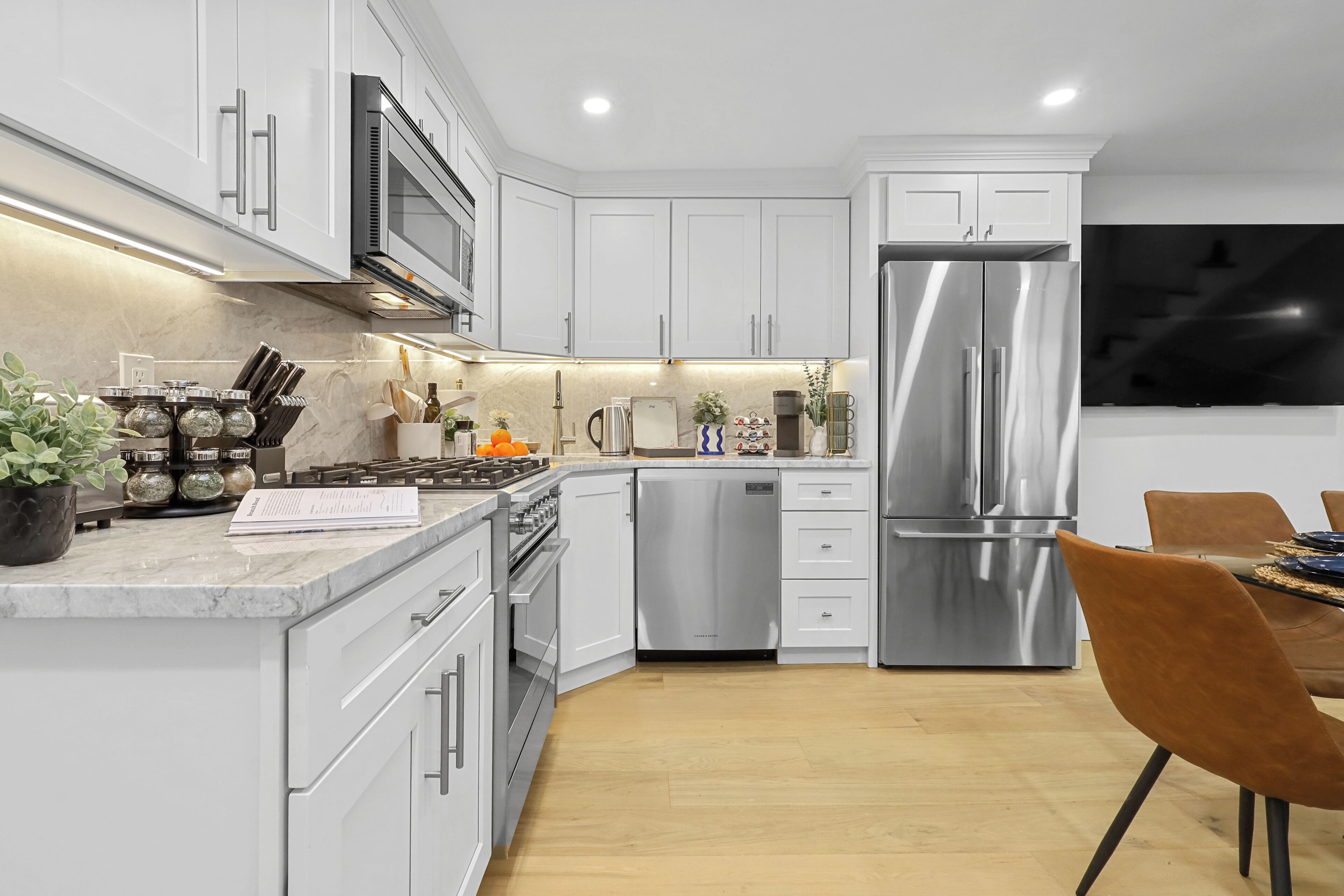 A modern kitchen with white cabinets, stainless steel appliances, and a wooden dining table with a brown chair.