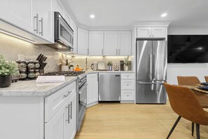 A modern kitchen with white cabinets, stainless steel appliances, and a wooden dining table with a brown chair. - North End Entire House / Heart of Boston (Boston)