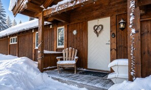 A wooden cabin with a white door, a heart-shaped decoration, and a bench outside. - The Cozy Family Mountain Retreat (Nybergsund)