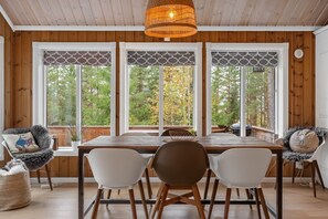 A dining area with a wooden table and chairs, large windows with decorative screens, and a hanging light fixture. - The Cozy Family Mountain Retreat (Nybergsund)
