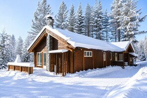 A wooden cabin with a stone chimney, surrounded by snow-covered trees. - The Cozy Family Mountain Retreat (Nybergsund)