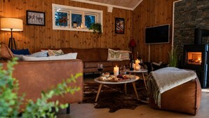 Een gezellige woonkamer met een bank, een bijzettafeltje met lekkernijen, een open haard en een aan de muur bevestigde televisie.