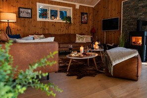 A cozy living room with a sofa, a coffee table with snacks, a fireplace, and a TV mounted on the wall. - The Cozy Family Mountain Retreat (Nybergsund)