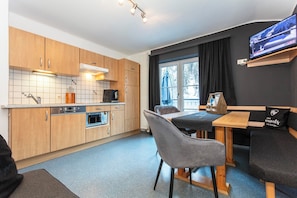 A compact kitchen with modern appliances, a dining area with a table and chairs, and a television mounted on the wall. - Gruber's Gästehaus - Ferienwohnungen (Viehhofen)