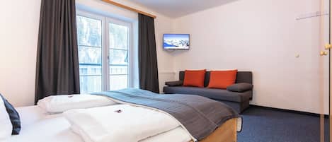 A hotel room with a bed, a sofa, a TV, and a window with curtains.