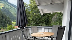 A balcony with a round table and chairs, a black umbrella, and a view of a green landscape. - Gruber's Gästehaus - Ferienwohnungen (Viehhofen)