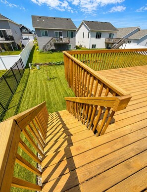 Une terrasse en bois avec des garde-corps, une pelouse bien entretenue et des maisons résidentielles en arrière-plan.