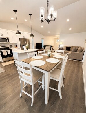 A modern kitchen with white cabinetry, a stainless steel refrigerator, and a dining area with a wooden table and white chairs.