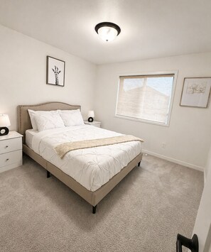 Une chambre à coucher comprenant un lit, des tables de chevet, une commode, une fenêtre et un luminaire au plafond.