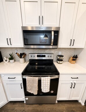 A kitchen with white cabinets, a stainless steel microwave, and a black stove with a towel hanging on the oven door.