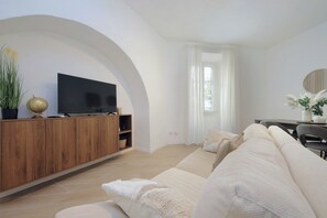 Ein modernes Wohnzimmer mit Flachbildfernseher auf einem Holzkabinett, einem großen Bogenfenster und einem beigefarbenen Sofa.