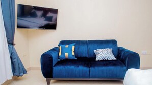 Una habitación con un sofá azul, un televisor montado en la pared y una cortina.