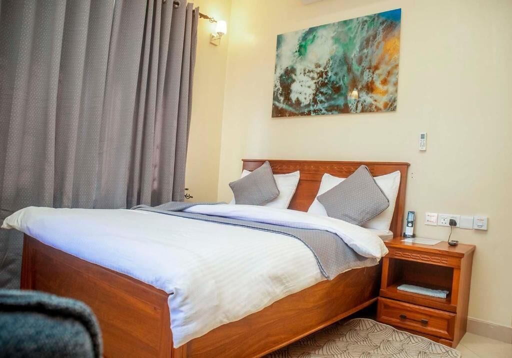 Habitación de hotel con cama de madera, una mesita de noche, un cuadro en la pared y una ventana con cortinas.