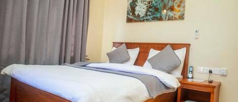 Een hotelkamer met een houten bed, een nachtkastje, een aan de muur hangend kunstwerk en een raam met gordijnen.
