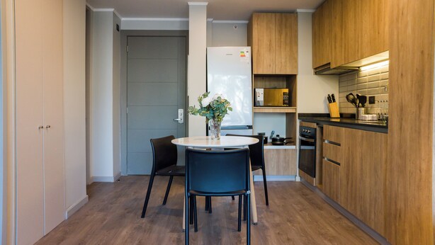 Et moderne køkken med træskabe, indbygget ovn og et spiseområde med bord og stole.