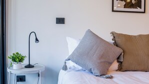 Et moderne soveværelse med seng, natbord, lampe og et billede i ramme på væggen.
