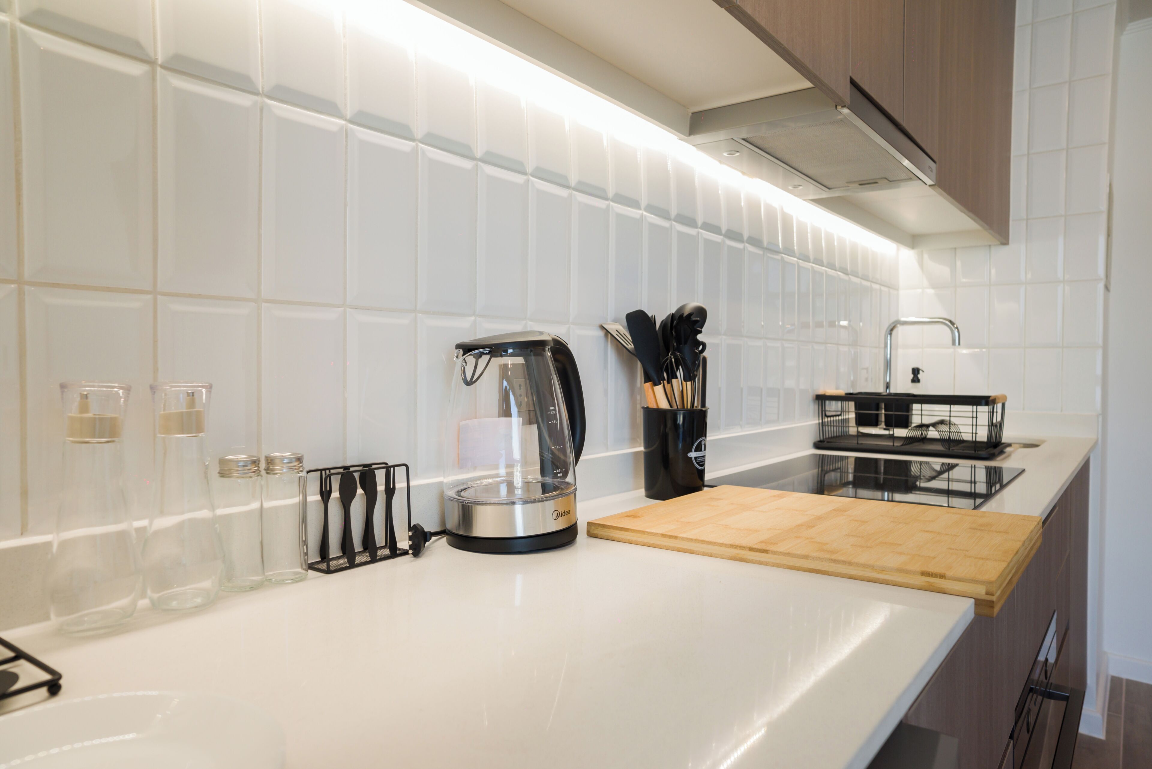 Una cocina moderna con azulejos blancos, cafetera, tabla de cortar y utensilios.
